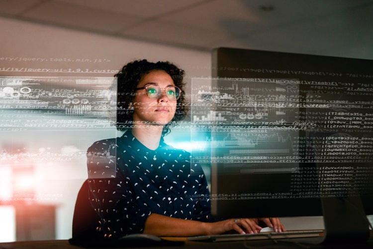 A focused woman interacts with an illuminated digital display, showcasing programming code and futuristic graphics, in a low-light environment, illustrating innovation and expertise.